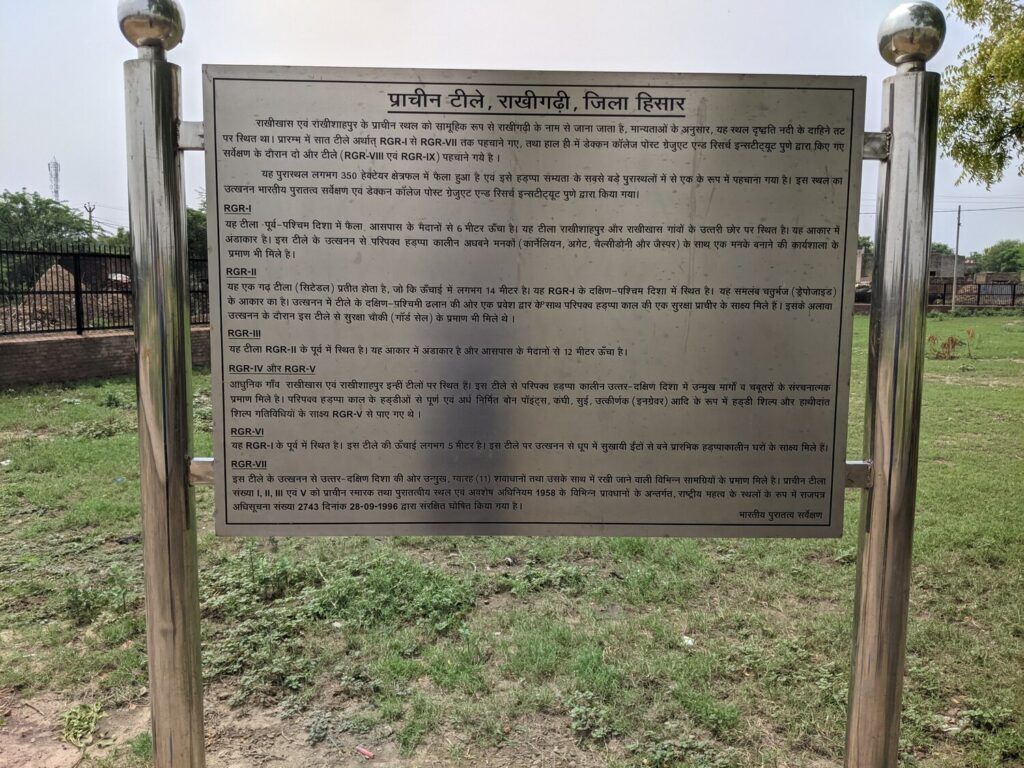 An archaeological site Rakhigarhi fenced off with a notice advising visitors to wait a few years due to ongoing construction.